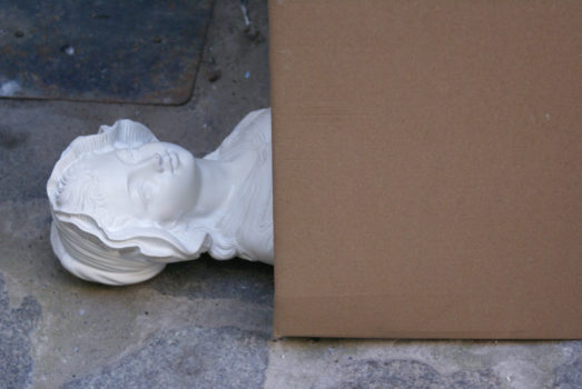 wyrzeźbione popiersie kobiece wystaje z leżącego kartonu na kostce brukowej w zbliżeniu