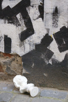 wyrzeźbione popiersie kobiece leży na ziemi na tle odrapanej czarno - białej ściany