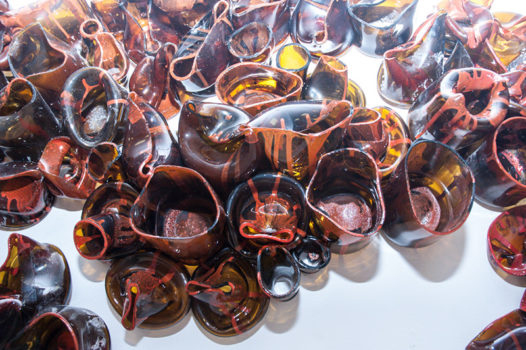 Zdjęcie fragmentu instalacji szklanej. Zdeformowane amorficzne  brązowe elementy ociekają czerwoną farbą.