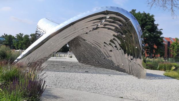 błyszcząca metalowa rzeźba - forma w przestrzeni miejskiej w kształcie łuku