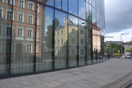 W szklanej elewacji współczesnego budynku odbija się zabudowa kamienic przy placu Strzeleckim.